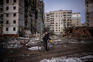 Мужчина едет на велосипеде между жилыми домами, пострадавшими во время обстрела в Чернигове. 4 марта 2022 года