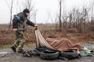 Член территориальной обороны Украины приподнимает ткань, которой накрыты четверо мирных жителей на обочине шоссе под одеялом в 20 километрах от Киева.