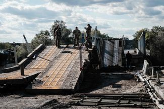 Украинские военные осматривают разрушенный мост через Северский Донец в освобожденном Изюме