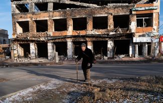 Пожилая жительница Изюма возле одного из разрушенных зданий в городе