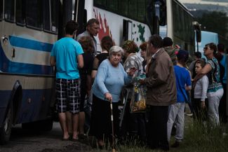 An elderly woman stands in a crowd of refugees near a bus. Izyum, Kharkiv region. June 13, 2014.