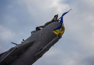 Боец ВСУ устанавливает флаг Украины на списанном истребителе, который превратили в памятник