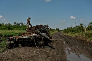 Украинский военнослужащий осматривает подбитый российский танк