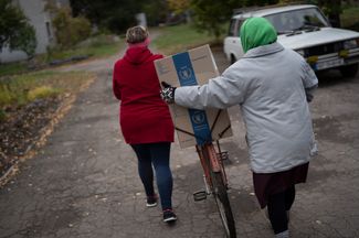 Жительницы Михайло-Лукашево везут коробку с гуманитарной помощью на велосипеде
