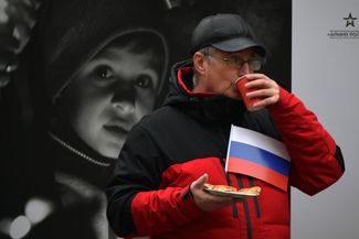 Житель Санкт-Петербурга во время празднования Дня народного единства в городе. Мужчина стоит на фоне одной из фотографий, демонстрируемых на выставке, посвященной жителям Донбасса