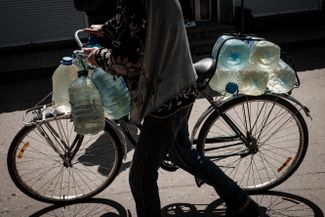 Житель Торецка ведет велосипед, груженный бутылками с водой. Город находится под обстрелами с начала марта.