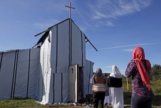 Мигранты-христиане из Эритреи и Эфиопии идут на воскресную службу в импровизированную церковь в лагере