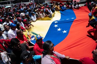 Сторонники Мадуро несут флаг страны во время марша против экономических санкций, введенных США. Сентябрь 2023 года