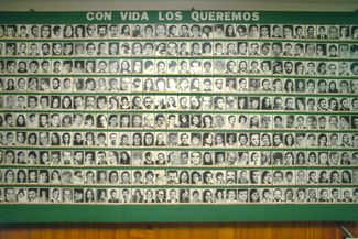 Стенд с фотографиями пропавших детей в помещении организации «Матери пропавших без вести». Над портретами надпись — «Мы хотим, чтобы они были живы»