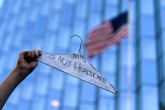 Женщина держит вешалку со словами «Это не здравоохранение», символизирующую небезопасные, незаконные аборты, во время акции протеста в Лос-Анджелесе