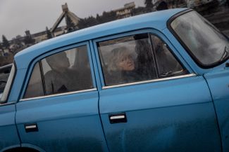 Пассажиры автомобиля в Тростянце смотрят на подбитый российский танк