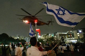 Израильтяне встречают вертолет с освобожденными заложниками, который прибывает в больницу города Петах-Тиква, 26 ноября 2023 года