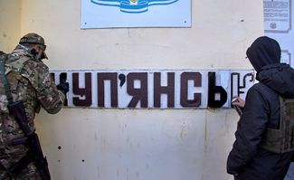 Солдат ВСУ и уличный художник заново пишут название города — на украинском языке. Российские силы во время оккупации Купянска исправили его на русский
