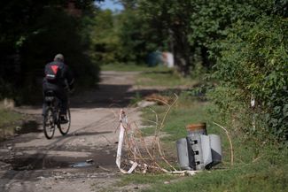 Мужчина проезжает на велосипеде мимо ракеты, застрявшей в земле в жилом районе Славянска