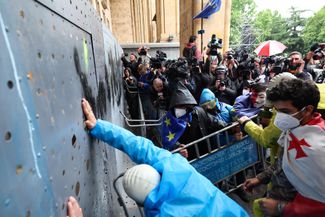 Демонстранты пытаются прорваться в парламент через металлический барьер, установленный перед главными воротами здания. 14 мая 2024 года