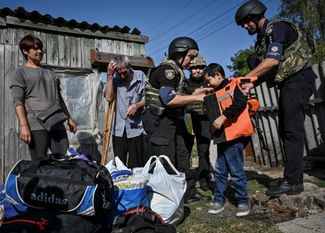 Полицейские надевают бронежилет на десятилетнего Дмитрия перед эвакуацией из поселка Степногорск рядом с линией фронта в Запорожской области