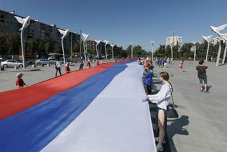 Местные жители, пророссийские активисты и сотрудники назначенной Кремлем городской администрации держат 100-метровый триколор на центральной площади оккупированного Мариуполя
