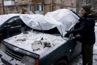Киевляне накрывают свой автомобиль, поврежденный во время атаки российских беспилотников