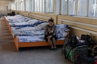 A displaced woman from Nagorno-Karabakh sits on a bed in a temporary shelter. Artashat, Armenia. October 6, 2023.