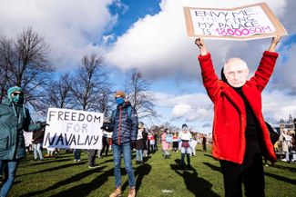 Протестующие слева держат плакат «Свободу Навальному» напротив российского торгпредства, протестующий справа в маске Владимира Путина поднял над головой плакат «Завидуй мне, король! У меня дворец на 18 тысяч квадратных метров». Амстердам, Нидерланды