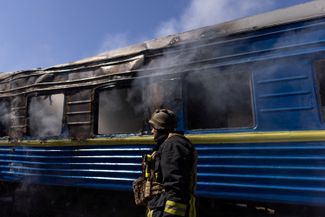 Украинский пожарный на фоне поезда, поврежденного в результате российской ракетной атаки по железнодорожному вокзалу Херсона 3 мая 2023 года