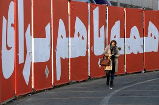 Иранка идет вдоль надписи «Все вместе за родину». 4 марта 2024 года