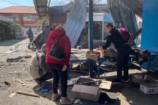 Мирные жители собирают уцелевшие товары на рынке после обстрела
