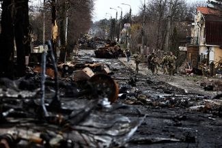 Украинские военные идут мимо подбитого российского танка и бронетехники в Буче. 2 апреля 2022 года
