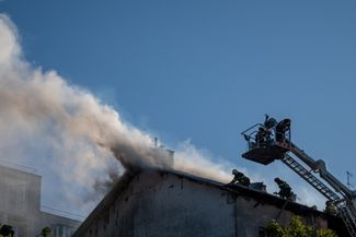 Пожарные тушат огонь на крыше здания, загоревшегося во время обстрела