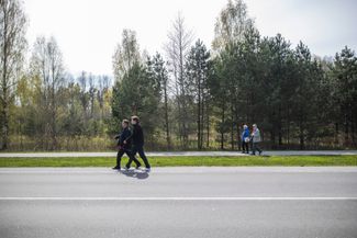 Жители Эстонии с цветами в руках идут по обочине к месту, где стоял Т-34