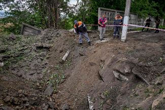 Работники коммунальных служб обследуют кратер, оставшийся после российского обстрела в Харькове в ночь с 2 на 3 августа