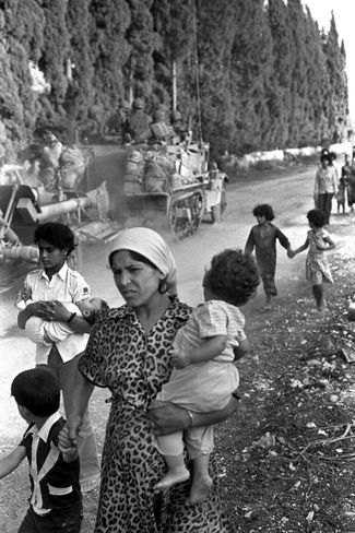 Israeli troops drive by residents of Sidon, Lebanon. June 9, 1982