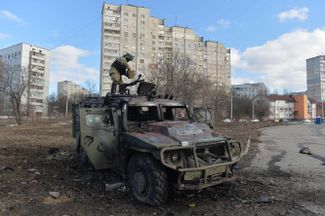 Боец территориальной обороны Украины осматривает подбитый в бою в Харькове бронеавтомобиль