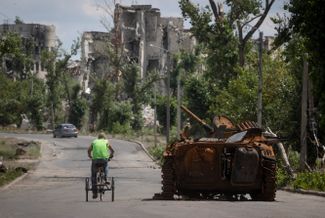 Житель города Рубежное Луганской области едет на велосипеде мимо сгоревшего танка. Рубежное занято вооруженными силами России, они вошли в агломерацию, куда входит город, в начале мая