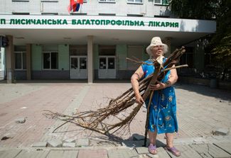 Женщина с охапкой дров у здания городской больницы в Лисичанске. Лисичанск был одним из последних городов Луганской области, который контролировали ВСУ. С конца апреля в городе отсутствовали газ, водо- и электроснабжение