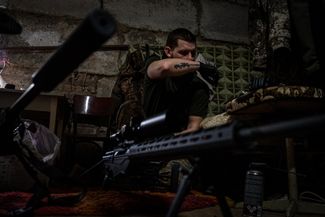 Военный Украинской добровольческой армии чистит снайперскую винтовку в подвале лагеря на позициях под Угледаром