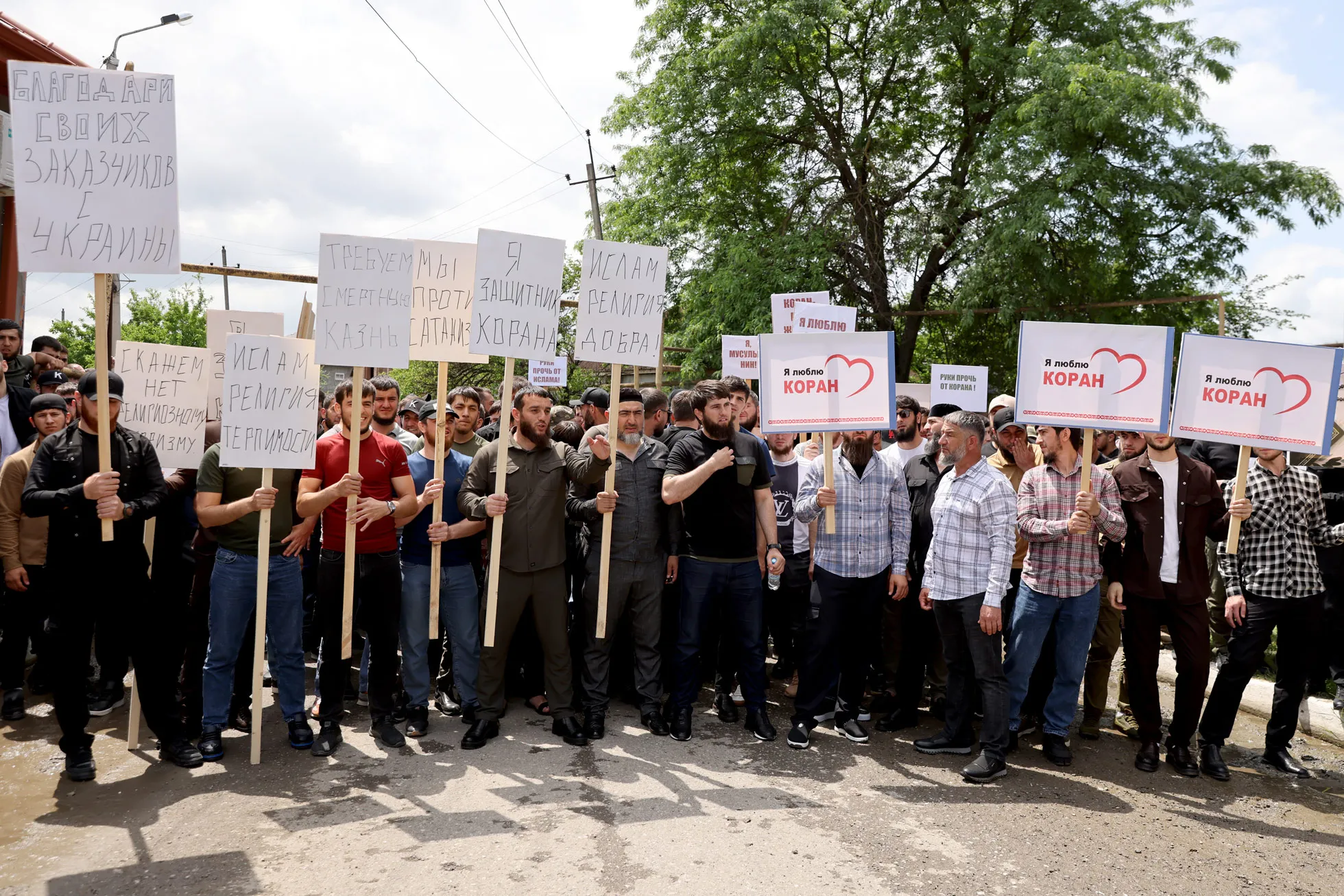 В Грозном волгоградца, арестованного по делу о сожжении Корана, встретили  плакатами «Мы требуем смертной казни» и «Ислам религия добра». Фотография —  Meduza