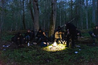 A group of refugees from Iraq rest in the middle of the forest. An activist provides basic first aid.