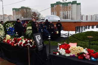 Navalny’s parents, Lyudmila and Anatoly, at his grave. Police can be seen on the roof of the apartment building in the background.