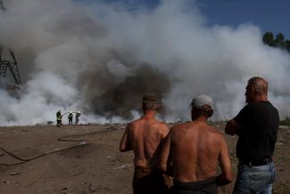 Жители Харькова наблюдают за пожарными, которые пытаются потушить возгорание, предположительно произошедшее в результате обстрела Немышлянского района в восточной части города