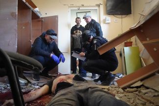 Сотрудники полиции осматривают тело мужчины, погибшего в результате налета российской авиации в Харькове, Украина
