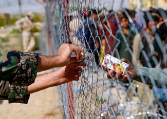 Иранский военный передает пачки сока через заграждение на ирано-афганской границе, за которым находятся беженцы из Афганистана. 19 августа 2021 года