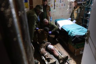 Украинские военные медики поднимают с носилок раненого под Бахмутом. 14 ноября 2023 года