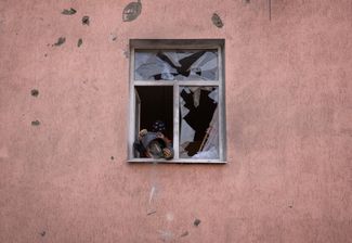 Жительница Краматорска выкидывает осколки стекла из окна своего дома, пострадавшего во время обстрела