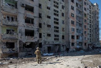 A Ukrainian soldier stands in front of a bombed-out residential building in Okhtyrka. March 24, 2022