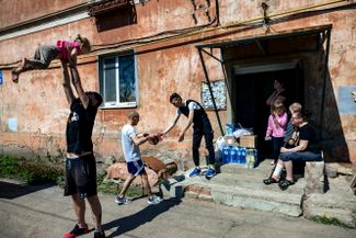 Трое украинцев доставляют гуманитарную помощь жителям города (один из них играет с ребенком). Они делают это каждый день на своем красном «опеле», из которого играет техно