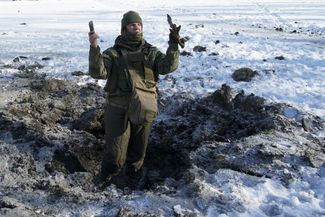 Украинский военный показывает куски шрапнели из ямы, образовавшейся после попадания снаряда, 31 января 2017 года