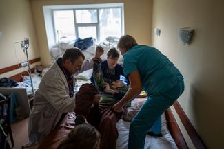 Доктора перекладывают пожилого пациента с носилок на кровать