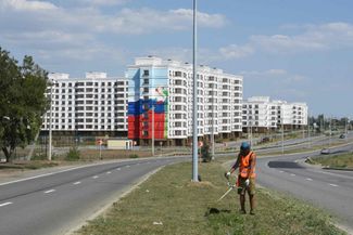 Рабочий стрижет газон вдоль дороги у новостроек в оккупированном Россией Мариуполе. 16 августа 2023 года