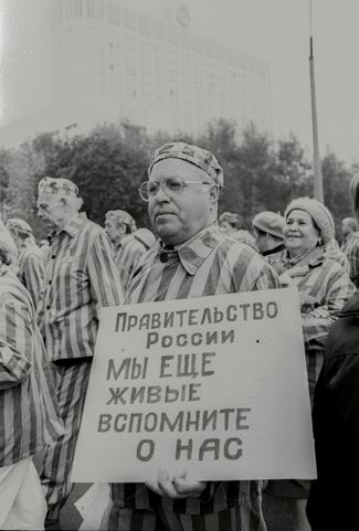 Бывший узник концентрационного лагеря с плакатом, обращенным к российскому правительству. Из-за тяжелой экономической ситуации многие пенсионеры остались без льгот и пенсий